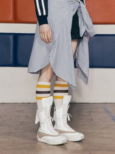 a person wearing white shoes and striped socks standing in front of a wall with orange stripes