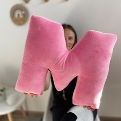 a woman holding a pink pillow in the shape of a letter m with her hands