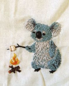 a small koala bear is holding a stick in it's hand while sitting next to a campfire