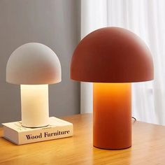 two lamps sitting on top of a wooden table next to a book and lamp shade