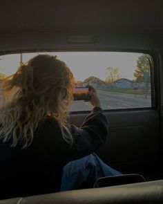 a woman sitting in the back seat of a car taking a photo with her cell phone