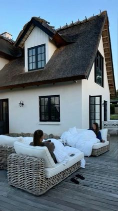 two people are sitting on wicker chairs in front of a house with thatched roof