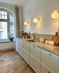 a kitchen with white cabinets and marble counter tops next to a large window in the corner