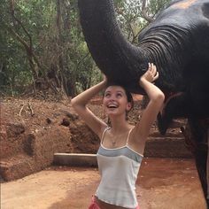 a woman standing next to an elephant with it's trunk over her head and smiling