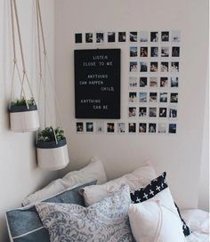 a bed with many pillows and pictures on the wall above it, along with hanging planters