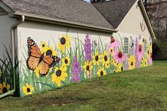 a painted mural on the side of a house with yellow and purple flowers in front of it