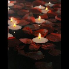 many lit candles are floating in the water with petals around them and on top of each other