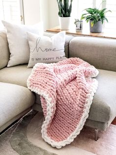 a pink knitted blanket sitting on top of a couch next to a pillow and potted plant