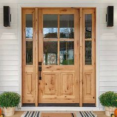 two potted plants are sitting on the front step of a white house with wooden doors