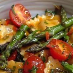 a white bowl filled with pasta, asparagus and tomatoes