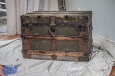 an old wooden chest sitting on top of a sheet of white paper next to a window