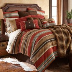 a bed covered in brown and red striped comforter next to a cowhide rug