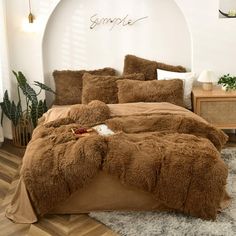 a bed with brown comforter and pillows in a room next to a plant on the floor