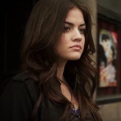 a woman with long brown hair standing in front of a building and looking off into the distance