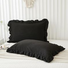 a bed with black ruffled pillows on top of it and a white wall in the background