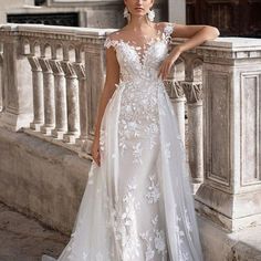 a woman in a white wedding dress standing on a balcony with her hand on her hip