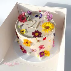 a white cake with colorful flowers on it in a box for someone's 21st birthday