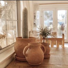 three clay vases sitting on top of a wooden table next to a glass window