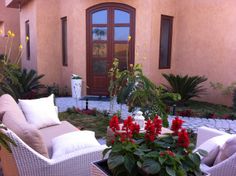 a patio with chairs and potted plants in front of a house that has red flowers on it