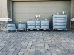 three blue dressers sitting next to each other on a brick floor in front of a garage