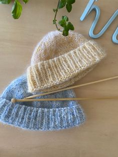 two knitted hats sitting on top of a wooden table next to plants and scissors