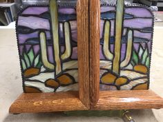 a stained glass and wood bookend with cactus designs on it's sides, sitting on a table