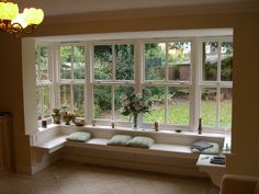 a window seat with pillows on it in front of a large window that looks out onto the yard