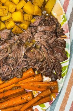 a plate full of meat, potatoes and carrots on a tablecloth with a striped towel