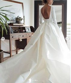 a woman in a white wedding dress is standing near a table with a potted plant