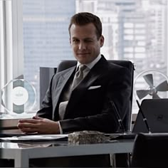 a man in a suit sitting at a desk with his hands folded and looking off to the side