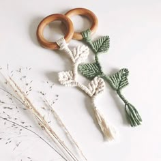 two crocheted wooden rings and some flowers on a white surface next to dried grass