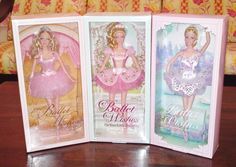 three barbie dolls in pink and white packagings on a wooden table next to a couch