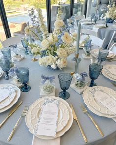 the table is set with blue and white plates, silverware, and flowers in vases