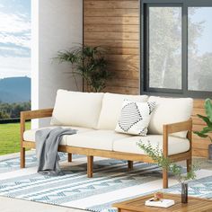 a white couch sitting on top of a wooden floor next to a window and potted plant