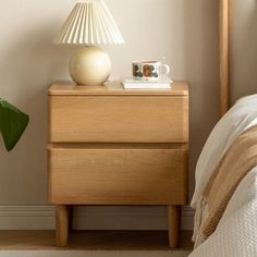 a nightstand with a lamp on top of it next to a bed and a plant