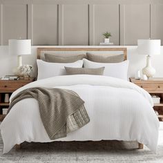 a bed with white sheets and pillows in a bedroom next to two lamps on either side of the bed