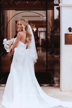 a woman in a white wedding dress is standing outside the entrance to a building with her bouquet