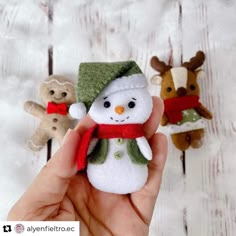 someone is holding three small snowmen in their hands, one wearing a green hat and the other a red scarf