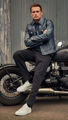 a man sitting on top of a motorcycle wearing a blue leather jacket and white sneakers