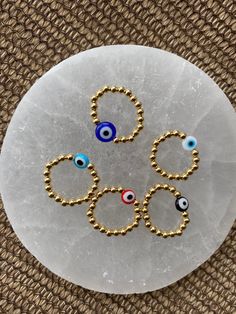 four evil eye charms on a white marble plate with gold beading and blue eyes