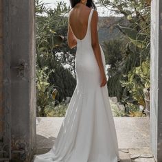 a woman in a white wedding dress looking out an open doorway at the trees and bushes