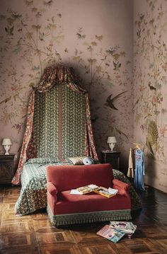 a red couch sitting next to a bed in a room with floral wallpaper on the walls