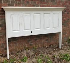 a white headboard on the side of a brick wall next to grass and dirt