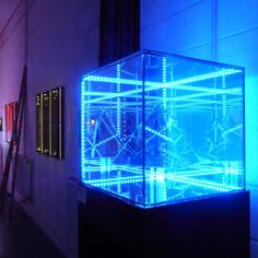 an illuminated cube in the middle of a room with other art pieces on the wall