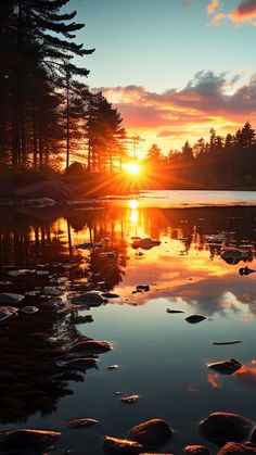 the sun is setting over a lake with rocks in front of it and trees on both sides