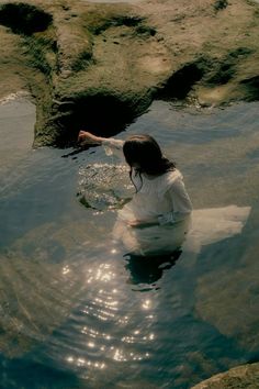 a woman sitting on top of a surfboard in the middle of water with rocks behind her