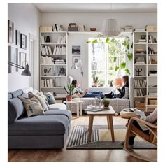 two people sitting in a living room with bookshelves and plants on the wall