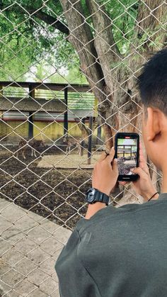 a man is looking at his cell phone while standing in front of a fenced area