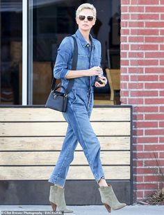 a woman walking down the street with a handbag on her shoulder and wearing blue denim overalls