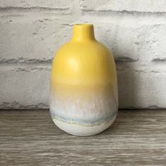 a yellow vase sitting on top of a wooden table next to a white brick wall